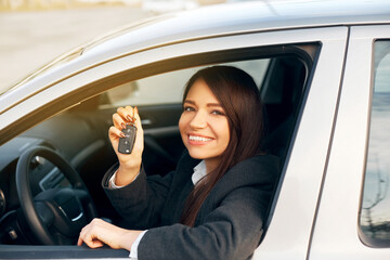 Happy young woman seated in her new car and showing car keys