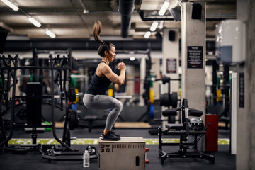A strong sportswoman is doing box jumps in a gym.