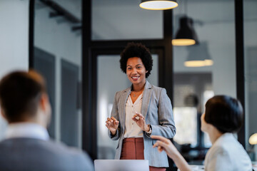 A confident interracial businesswoman is standing at the boardroom with employees and having...