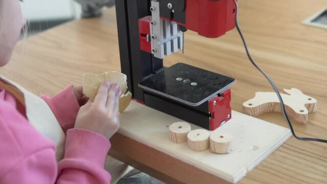 A little girl learns to make a toy out of wood in a master class
