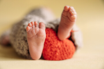 Legs of a newborn. Baby feet with a crochet heart. The tiny foot of a newborn in soft selective focus. High quality photo