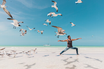 Man practicing yoga on the beach surrounded by seagulls