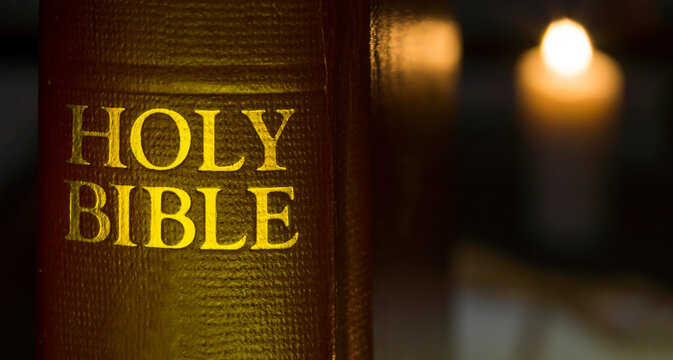 Holy Bible in close-up and a lit candle at the background disfocused