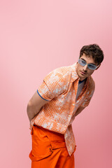 Young brunette man in sunglasses and shirt looking away isolated on pink.