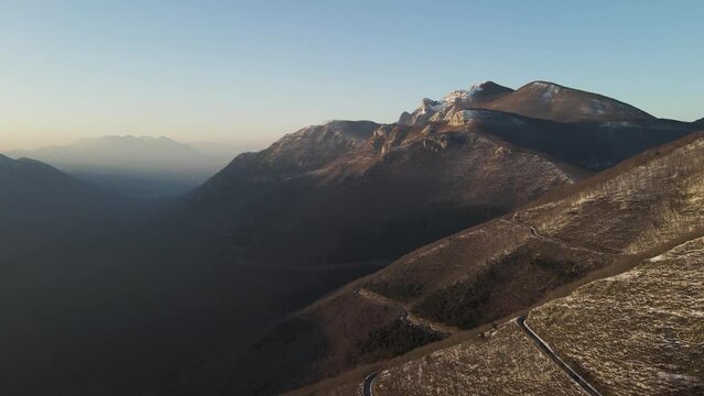 Aerial view of a scenic forest road on mountainside in wintertime at sunset with snow on Mount Terminio, Serino, Avellino, Irpinia, Campania, Italy.