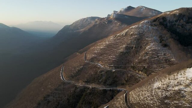 Aerial view of a scenic forest road on mountainside in wintertime at sunset with snow on Mount Terminio, Serino, Avellino, Irpinia, Campania, Italy.