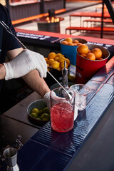 bartender stirs a cocktail with a bar spoon on a drain against the background of a bar with fruits, oranges and lemons on a summer sunny day