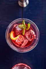 red summer cocktail with lemon and mint top view on blue brane stand, measuring cup, strainer, jiger