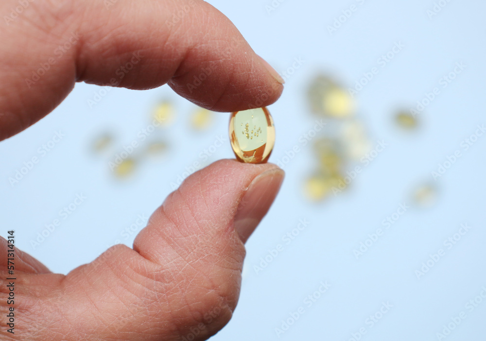 Wall mural Yellow capsule of fish oil in a male hand close-up.