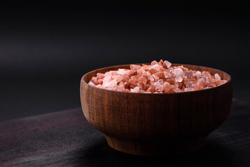 Fototapeta na wymiar Pink himalayan salt in a wooden bowl on a dark concrete background