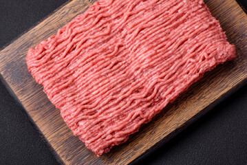 Raw beef or pork mince with salt spices and herbs on a wooden cutting board