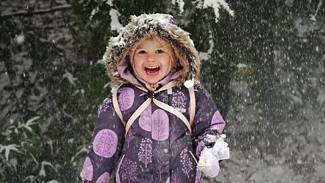 Snow falling and little girl, slow motion. Happy child rejoices in winter on snow tree background. The child plays with snow in Prague park.