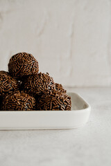 Brigadeiros de chocolate empilhados sobre prato de porcelana em fundo branco