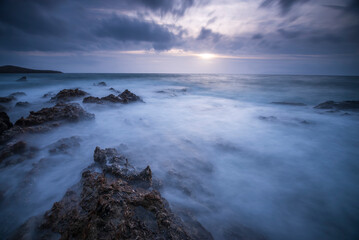 Long exposure shot of rocks on seaside, blurred and foggy sea water and clouds on sky