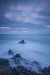Long exposure shot of rocks on seaside, blurred and foggy sea water and clouds on sky