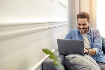 Young freelancer is smiling, typing on his laptop in nice modern home