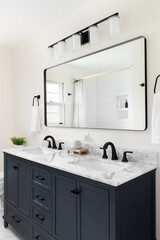 A beautiful bathroom with a dark blue vanity cabinet, marble countertop, and large mirror below a...