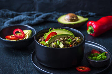 Lentil salad with avocado and red pepper in a black bowl on black background. Vegetarian and vegan food.