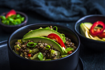 Lentil salad with avocado and red pepper in a black bowl on black background. Vegetarian and vegan...