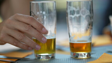 Two half full draft beers at restaurant table. Person hand closeup picking drink