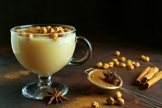 Close up of traditional turkish drink boza with cinnamon and roasted chickpea. Winter beverage in glass cup on black background. Copy space. Dark low key photo. Selective focus. Blurred background.