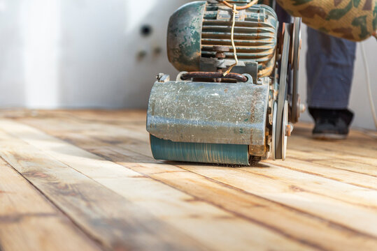 Worker polishing parquet floor with grinding machine.