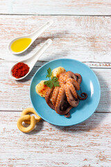 Galician style octopus on a blue plate with spoonfuls of olive oil and paprika. Typical Spanish food.