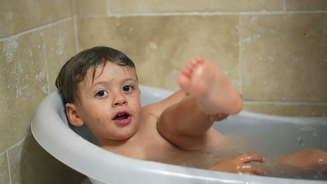 Cute baby bathing in small bathtub. Toddler boy washing routine bath tub