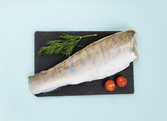 Raw pike perch fillet with fresh cherry tomatoes and a branch of dill on a black slate on a blue...