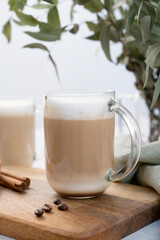 Сappuccino or latte with milk foam in glasses on a wooden plate with coffee beans, cinnamon and eucalyptus branch close up.