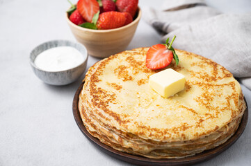 Sweet crepes stacked with butter, sour cream and fresh strawberries on a light background. The concept of homemade breakfast food.