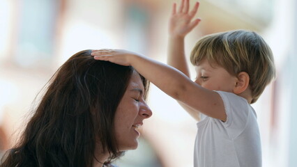 Naklejka premium Mischievous child hurting mother. Parenting concept of mom being hit in the head by 2 year old toddler boy. Terrible two concept. Childhood stress concept