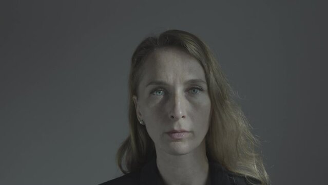 The attractive face of a woman emerges from the shadows into the light. Emphasis on the eyes. Caucasian with gray eyes.