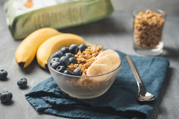 Granola cereal oatmeal with blueberries and banana fruits in a bowl on a blue napkin and grey background