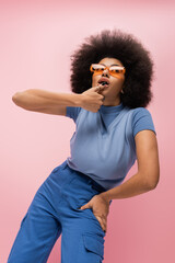 Trendy african american woman in sunglasses posing isolated on pink.