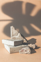 Stone showcase. Product presentation. Nature composition. Broken mineral rock pieces stand palm leaf shadow on beige empty space advertising background.