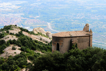 Fototapeta na wymiar An old chapel in yellow tones, seen from behind, overlooking the valley, lost in the midst of a mountain of stones and green vegetation.