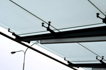 bus stop glazing. glass canopy attached at n several points to the metal structure. Gaps between the sky that have dots as protection against sunlight, overcast, rain, snow, station, platform