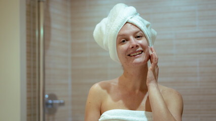 Young woman smiling while massaging her face in home bath, copy space, skin care routine
