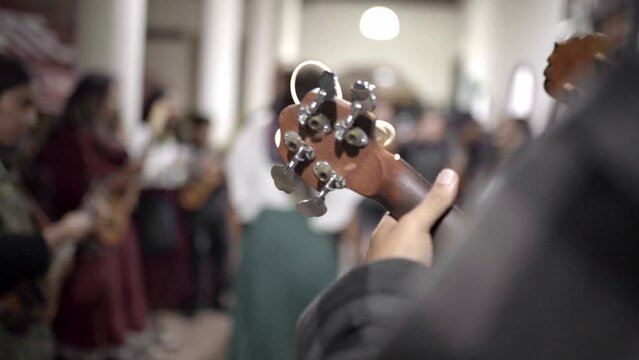 A mexican male musician playing jarana guitar with a couple dancing in the background