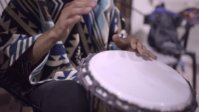 A young male playing djembe drums in a mexican jam session wearing a poncho