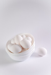 Fresh white eggs in a white porcelain bowl on a white table and white background, front view , copy space
