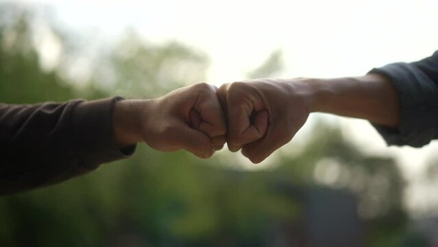 Close-up short of fist bump in green nature and sunlight background. Partnership power of teamwork concept. slow motion.