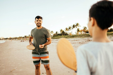 Father and son having fun on the beach during summer vacation playing beach tennis