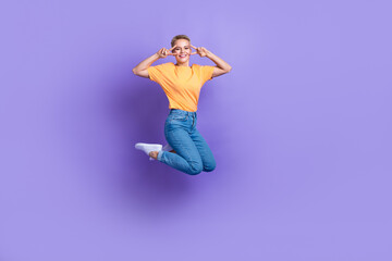 Fototapeta na wymiar Full size photo of overjoyed carefree girl jumping demonstrate v-sign near eyes isolated on violet color background