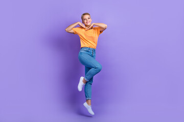 Fototapeta na wymiar Full size photo of gorgeous optimistic satisfied girl sneakers denim pants hold hands near face isolated on purple color background
