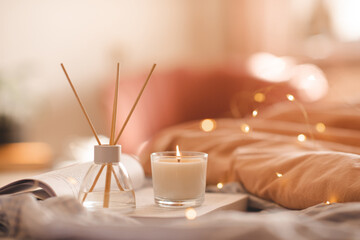 Liquid home perfume in glass bottle and bamboo sticks with scented candle stay on paper book in bed...