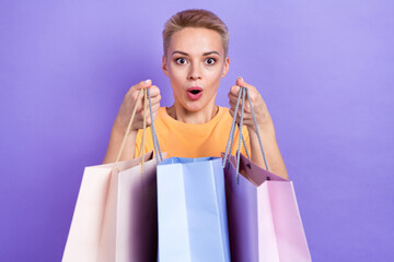 Fototapeta na wymiar Photo of lovely impressed girl with short hairdo dressed yellow t-shirt hold shopping bags open mouth isolated on purple color background