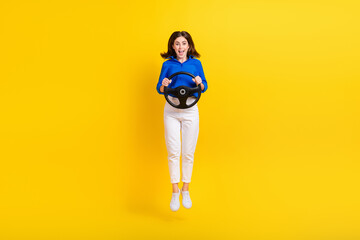 Fototapeta na wymiar Full length photo of sweet impressed girl dressed blue shirt car rider jumping high isolated yellow color background