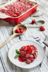 High angle view of sweet homemade strawberry cobbler or Sonker baked in a red ceramic pan over a rustic white wood table. Extreme selective focus with blurred background.